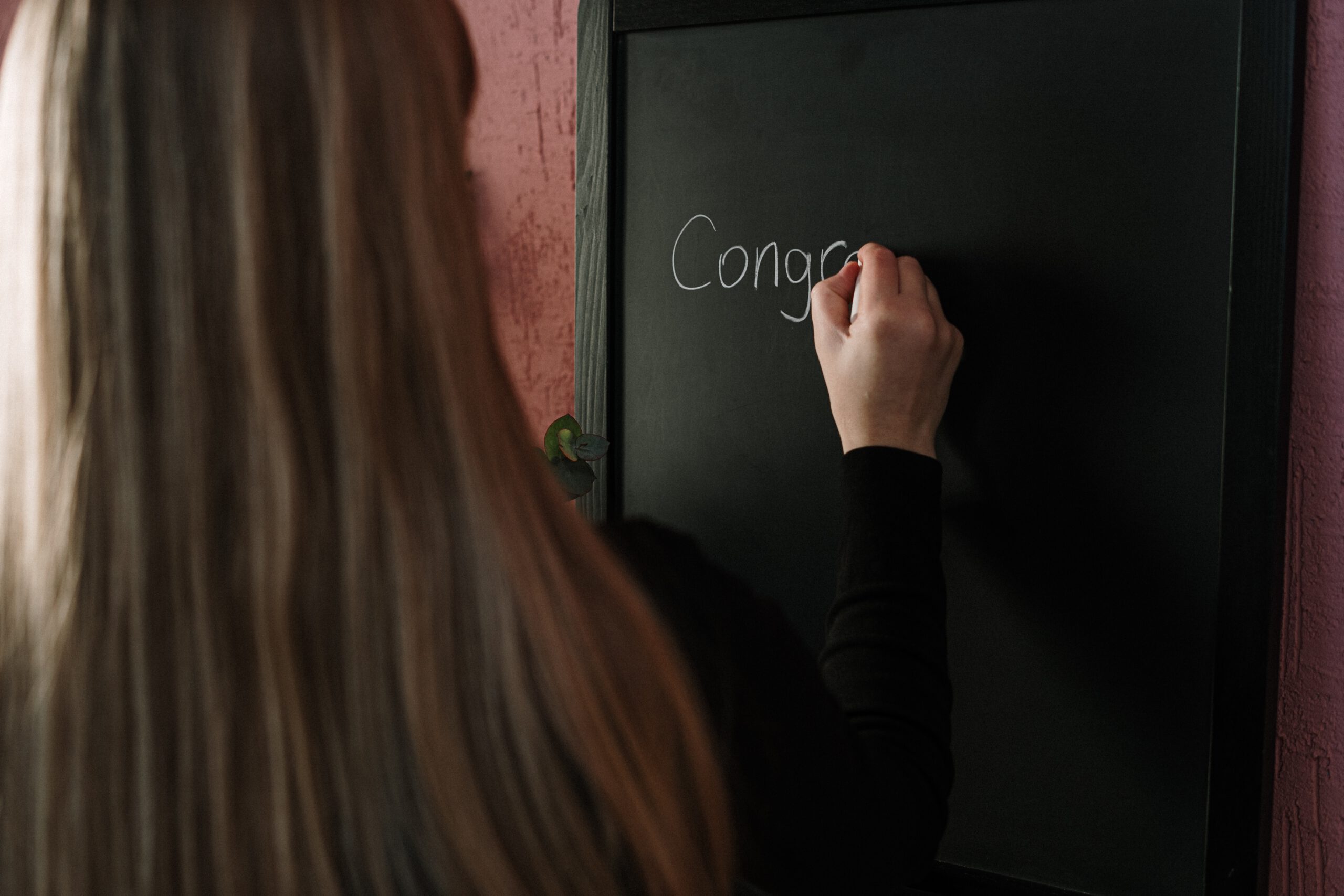 Dziewczyna pisząca na tablicy kredą słowo congratulations