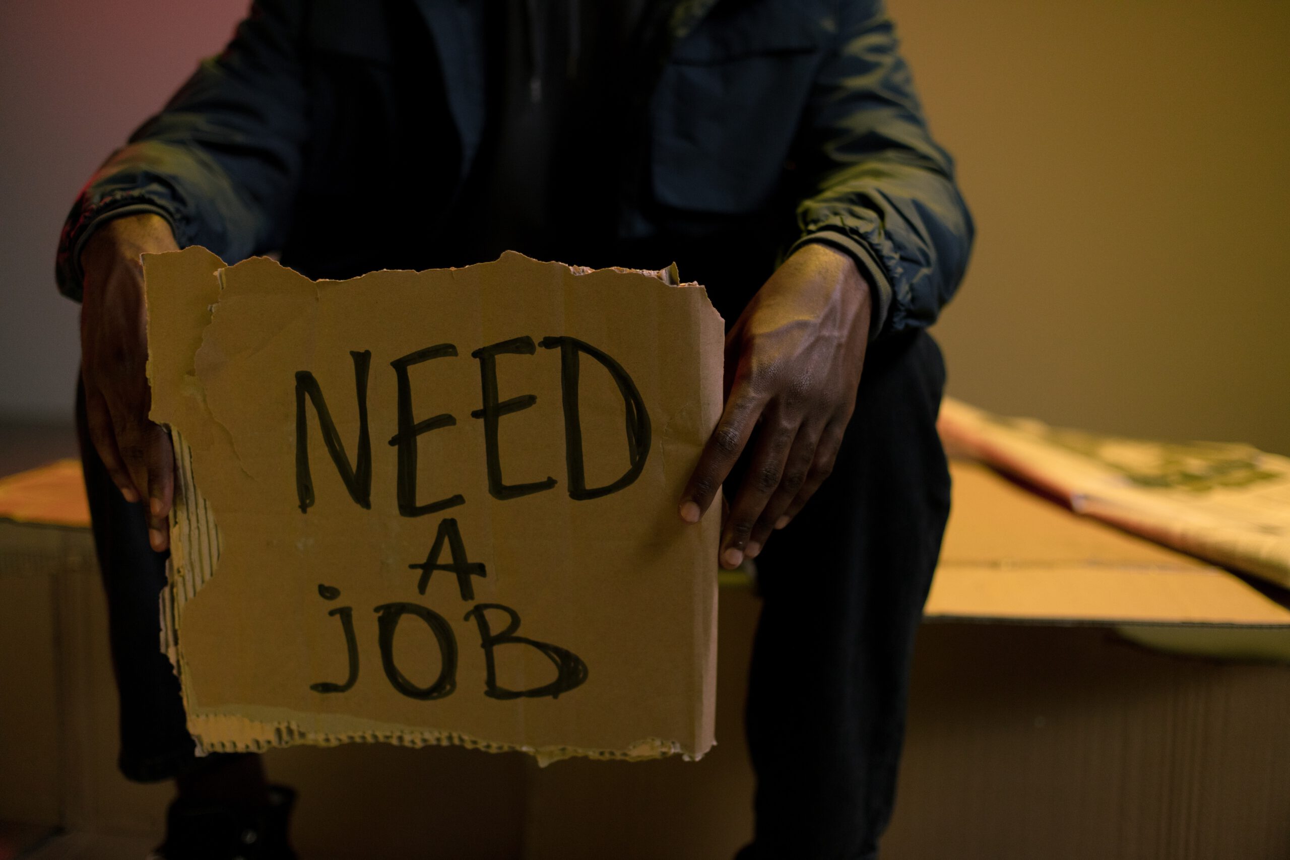 Mężczyzna trzymający przed sobą kartkę z napisem need a job