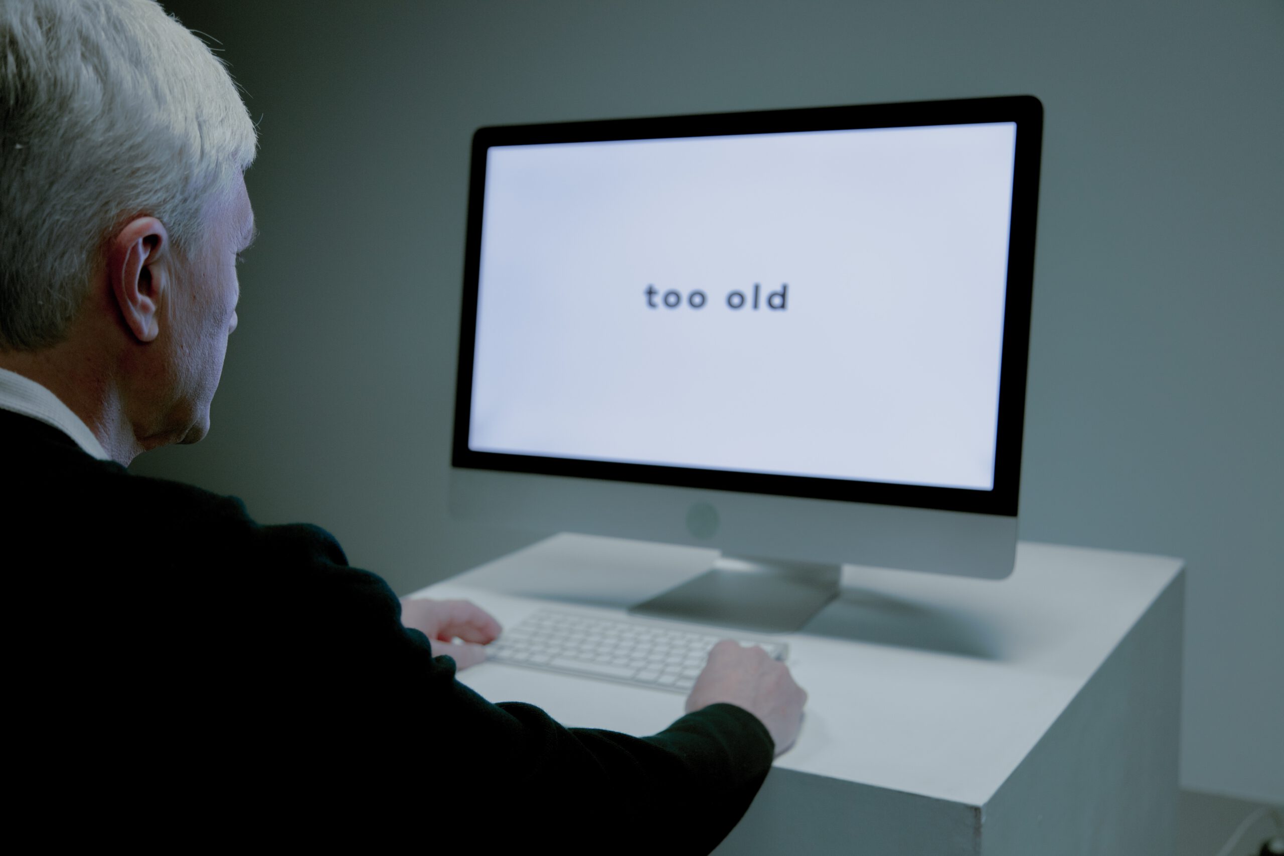 Starszy mężczyzn na bezrobociu siedzący przed ekranem komputera z wyświetlonym napisem too old